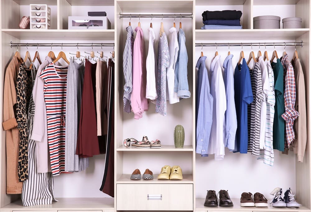 Organized wardrobe with hanging clothes, folded garments, shoes, and accessories neatly arranged on shelves and in drawers.